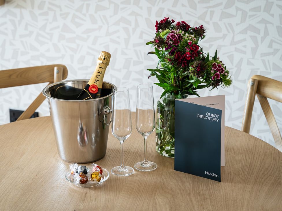A dining table with champagne, glasses, flowers, and a guest directory at Hidden 19- Coastal Hot Tub in St Ives