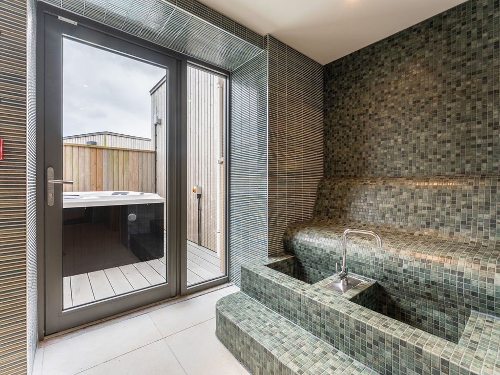 A bathroom with a hot tub and tiled seating area at Hidden 10- Godrevy View St Ives