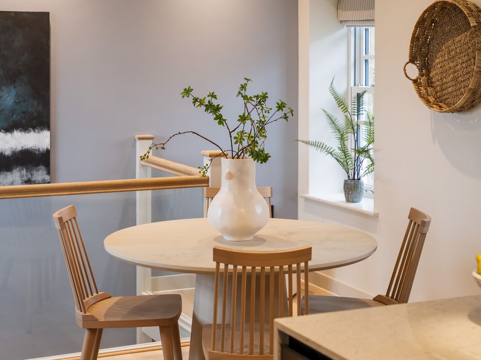 A dining room with a round table and a vase of branches at tbc in St. Ives