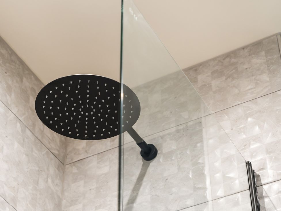 A shower head and glass panel in a bathroom at tbc St. Ives