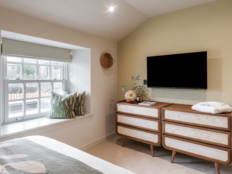 A bedroom with a window, cushions, television, and a drawer unit at tbc in St. Ives