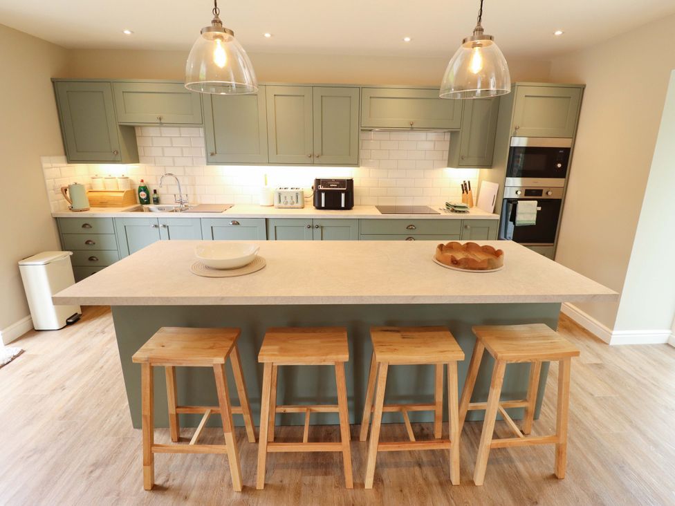 A kitchen with a kitchen island and bar stools at Bobblehat Barn in Alford