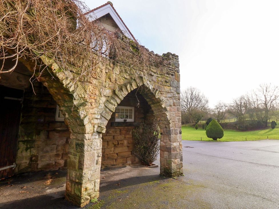 An outdoor view of a stone archway with trees and grass at The Bothy in Knaresborough