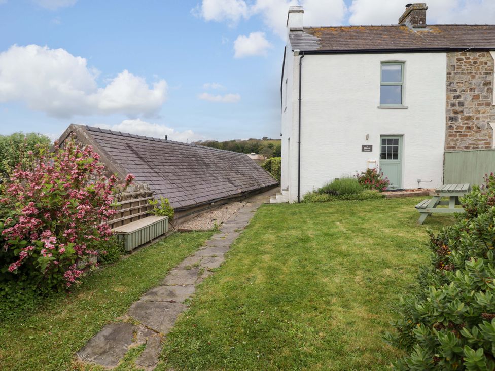 An outdoor view of a house with a path and flower bushes at No.8 Millmoor Farm Cottage in Broad Haven