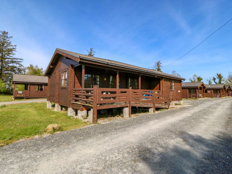 A wooden cabin with a porch and gravel road at Lodge 1 - Bron Eifion in Criccieth