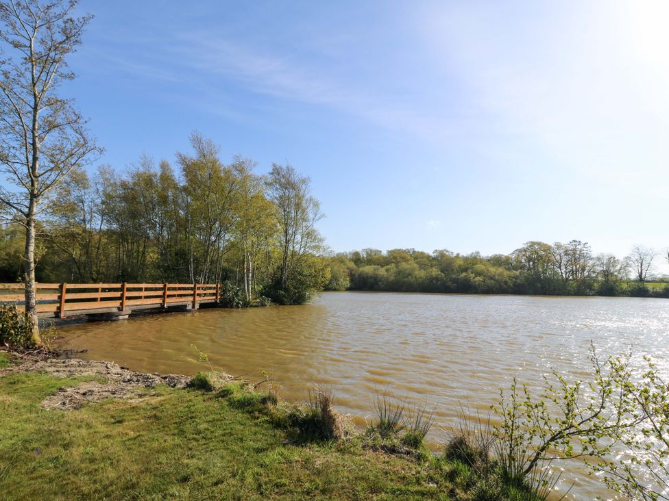A view of a lake with a wooden bridge and trees at Lodge 1 - Bron Eifion Criccieth