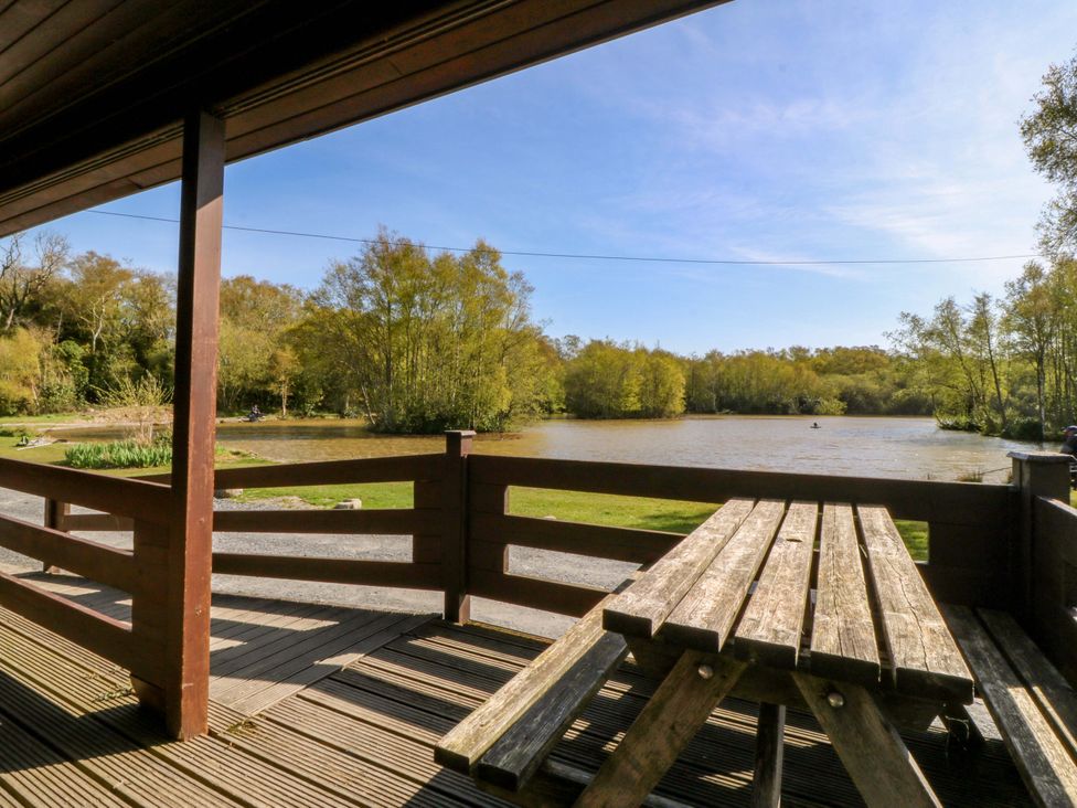 An outdoor area with a wooden table overlooking a lake at Lodge 2 - Bron Eifion