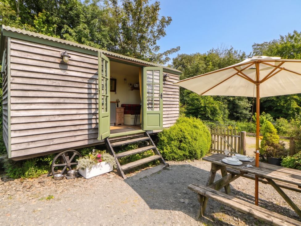 An outdoor seating area with a shepherd hut and table at The Three Spaniels Shepherds Hut Cwrtnewydd near Llanybydder