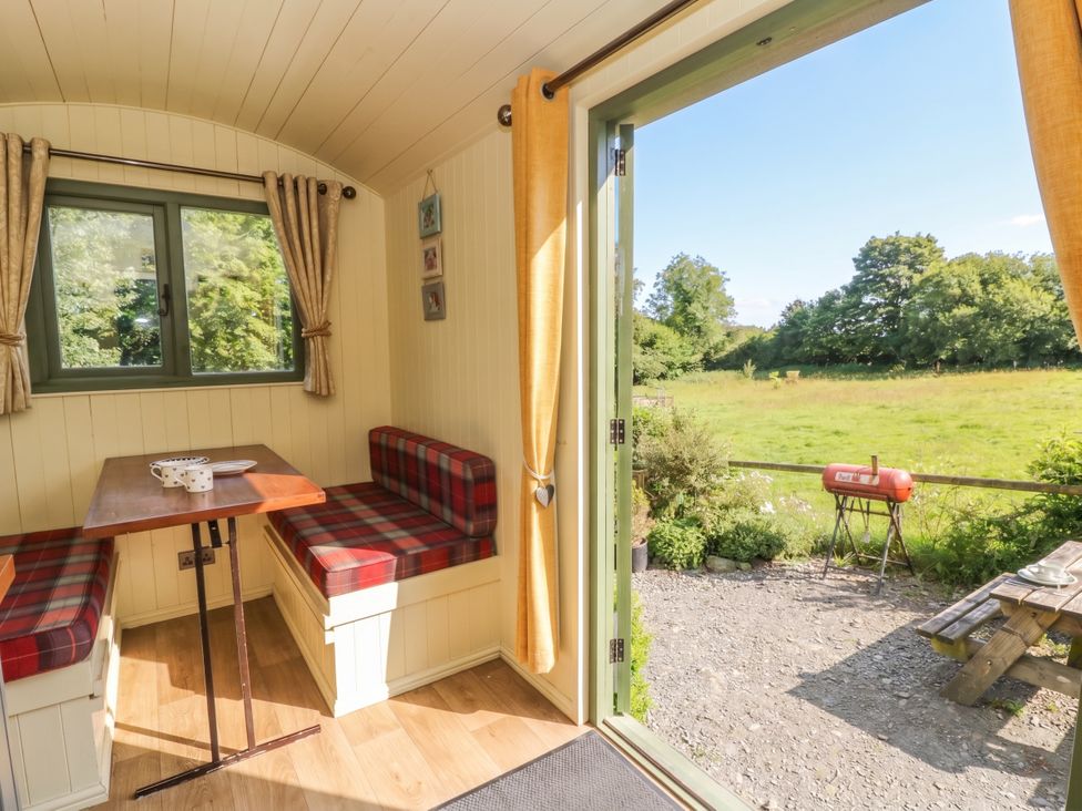 A dining area with a table and benches overlooking a garden at The Three Spaniels Shepherds Hut in Cwrtnewydd near Llanybydder