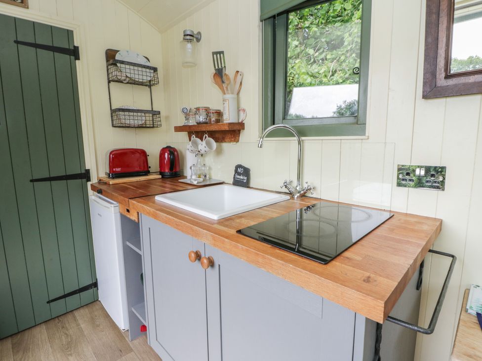 A kitchen with a sink, stove, and refrigerator at The Three Spaniels Shepherds Hut Cwrtnewydd near Llanybydder
