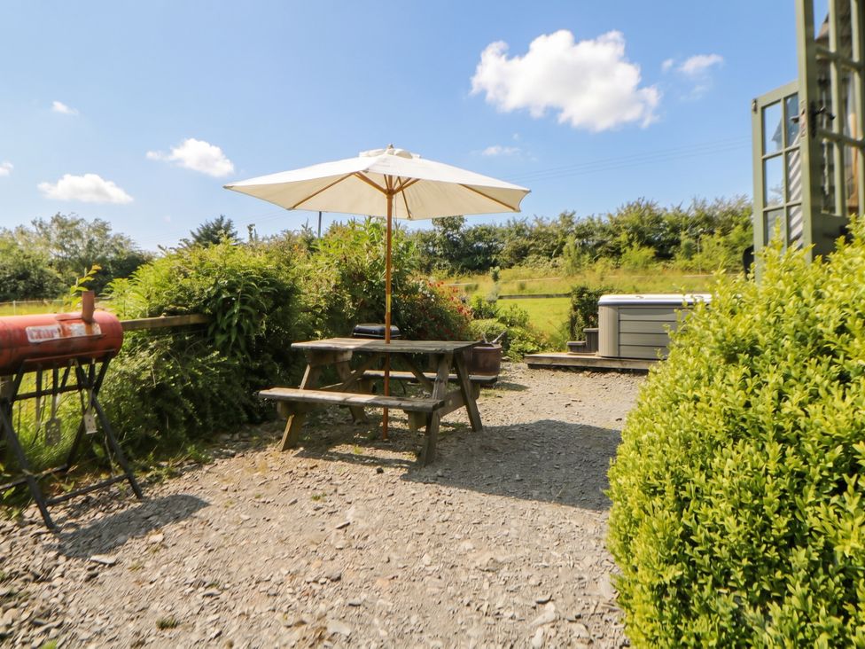 A picnic table with umbrella and hot tub at The Three Spaniels Shepherds Hut Cwrtnewydd near Llanybydder