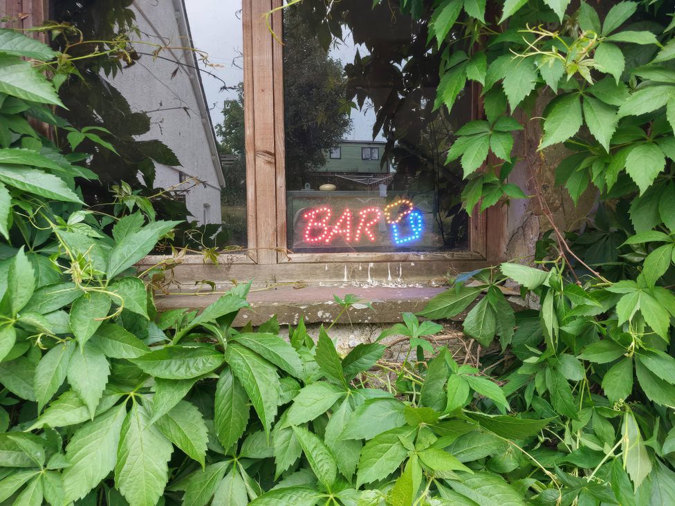 A window with a neon bar sign surrounded by green leaves at The Three Spaniels Shepherds Hut in Lampeter
