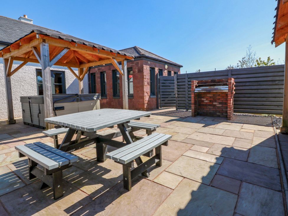 An outdoor area with a hot tub, table, benches, and barbecue at Ballaganlea in Alexandria