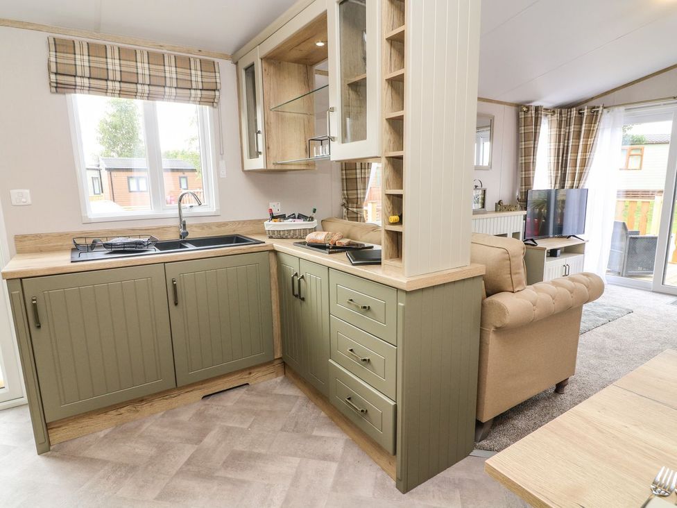 A kitchen with sink, stove, cabinets, and sofa at Hedgehog Lodge, Carnforth