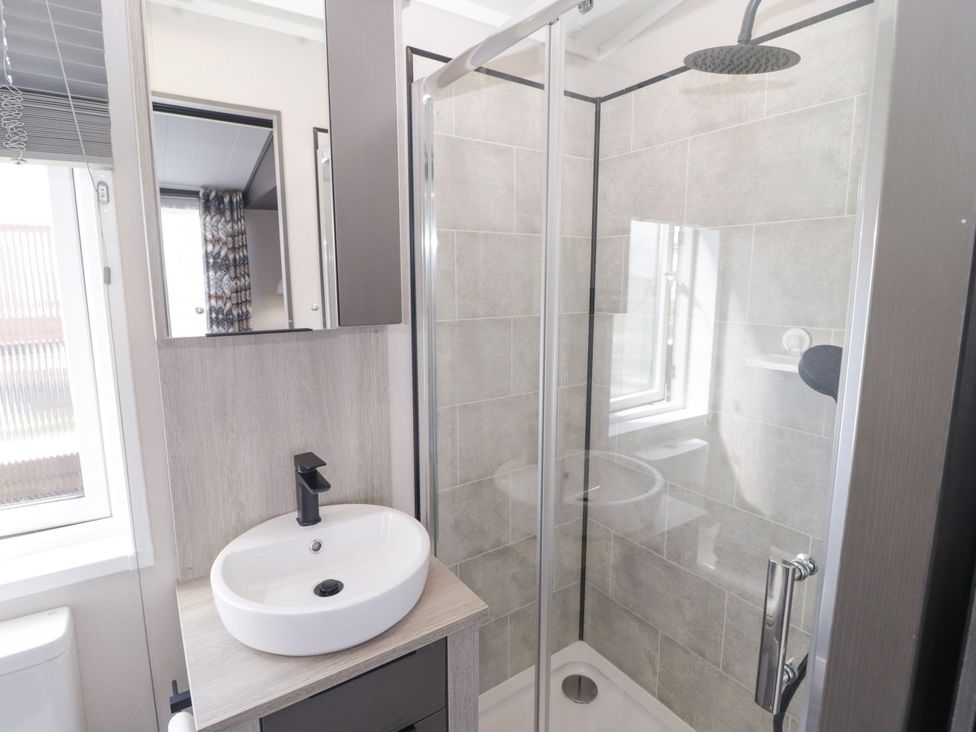 A bathroom with a shower, wash basin, and toilet at Stone Crab Lodge in Haverfordwest