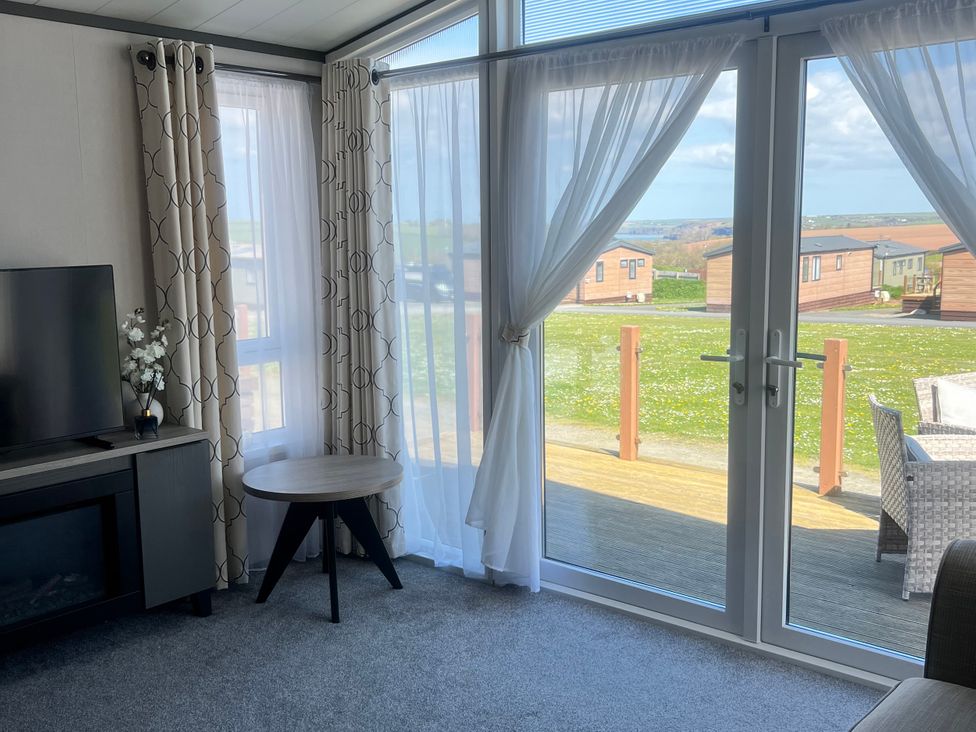 A living room with a TV and curtains at Stone Crab Lodge Hasguard Cross near Broad Haven
