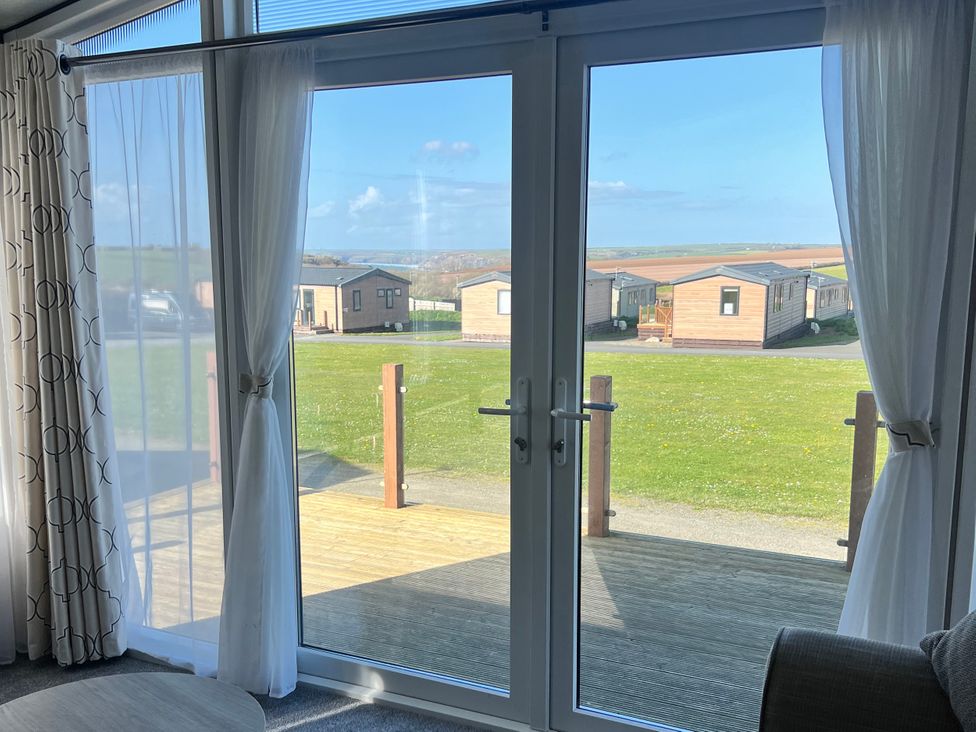 A living room with sliding doors and a view of holiday homes at Stone Crab Lodge Hasguard Cross near Broad Haven