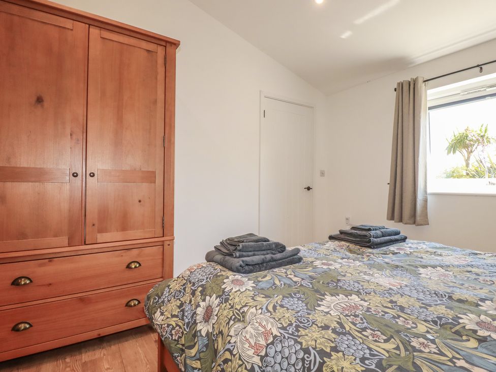 A bedroom with a wardrobe and bedding at Wisteria Lodge Redruth