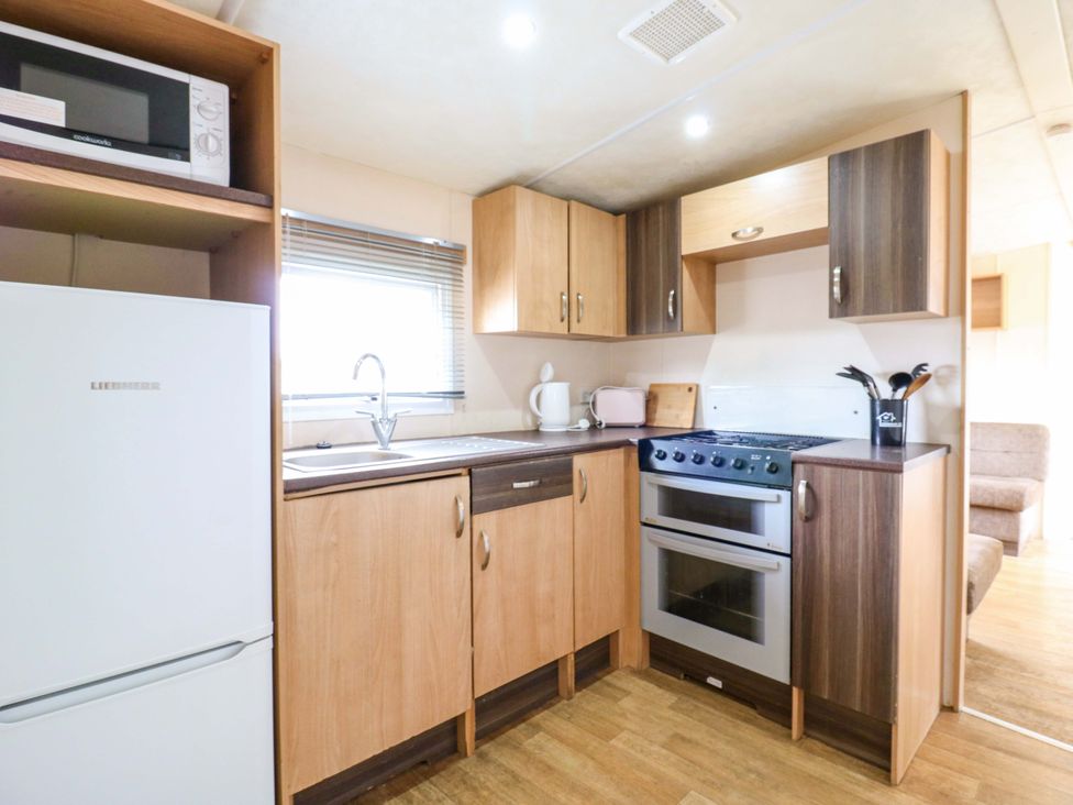 A kitchen with refrigerator, sink, stove, and microwave at Caravan 102 seawick Clacton-on-Sea