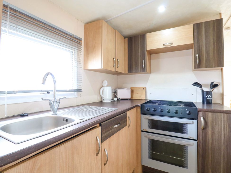 A kitchen with cabinets, sink, stove, and appliances at Caravan 102 seawick in Clacton-on-Sea