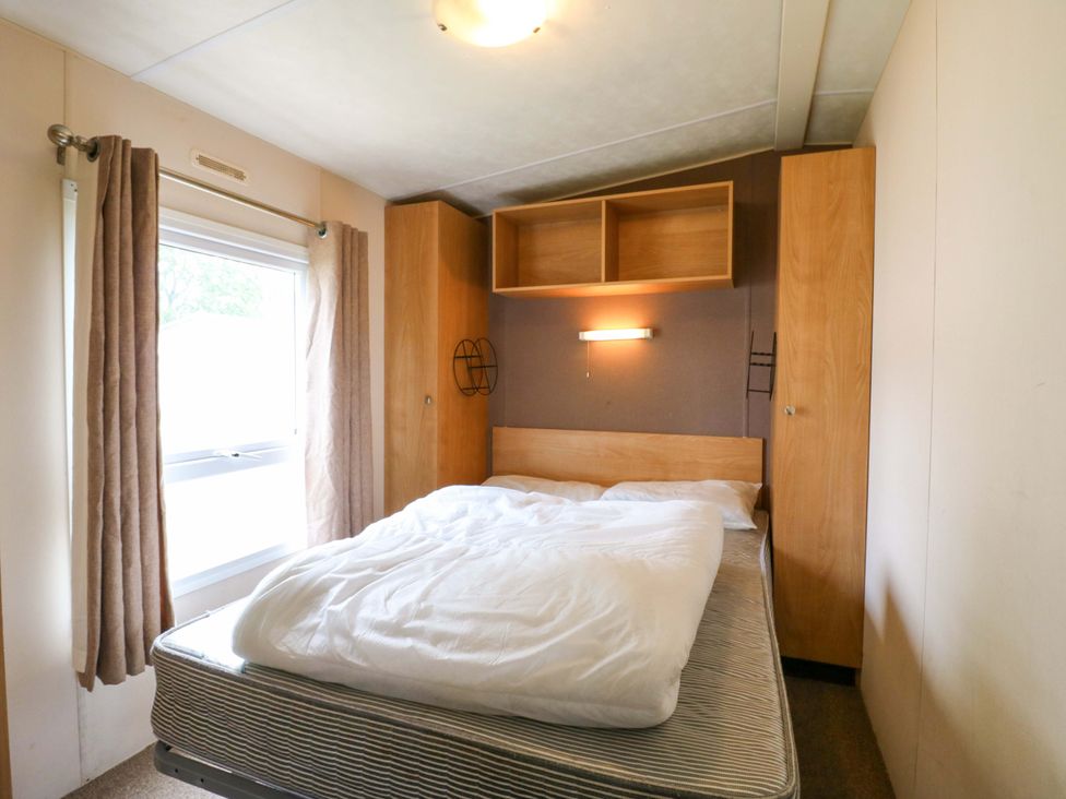 A bedroom with a bed and curtains at Caravan 102 seawick in Clacton-on-Sea