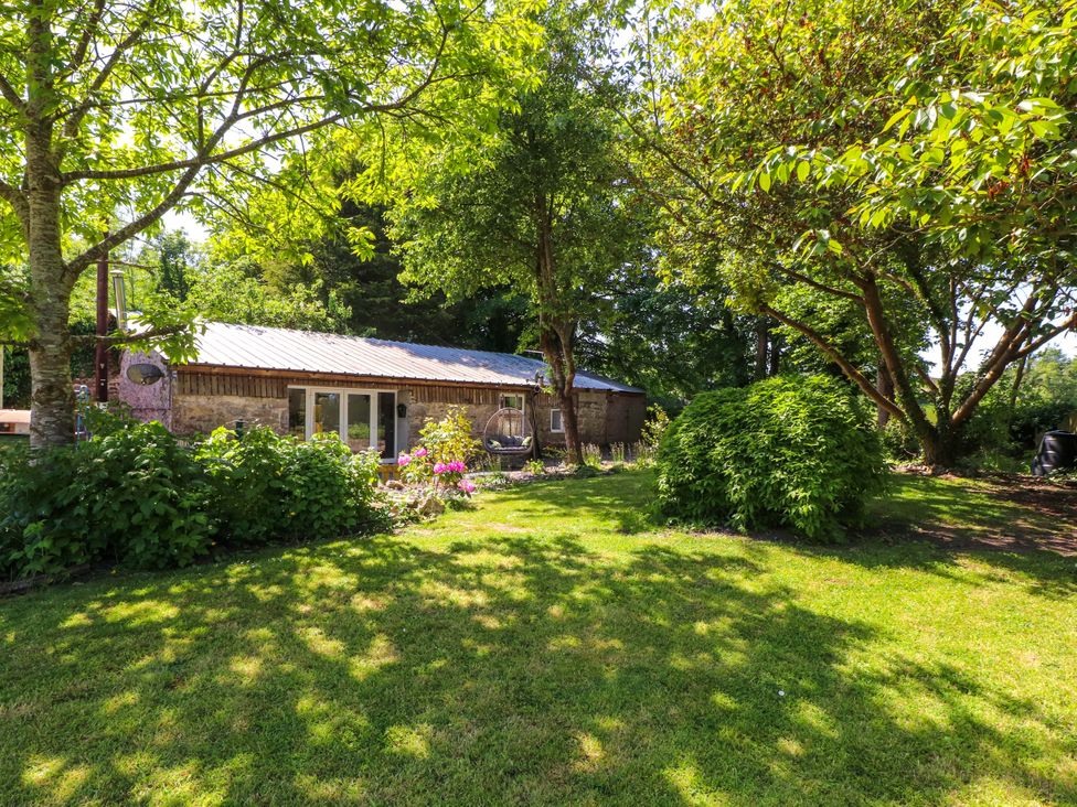 A garden with a building and greenery at Woodman's Lodge in Llanallgo near Moelfre