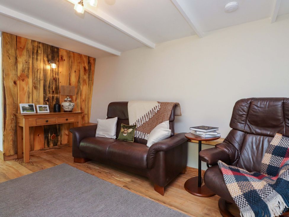 A living room with a sofa and armchair with a side table at Woodman's Lodge in Llanallgo near Moelfre