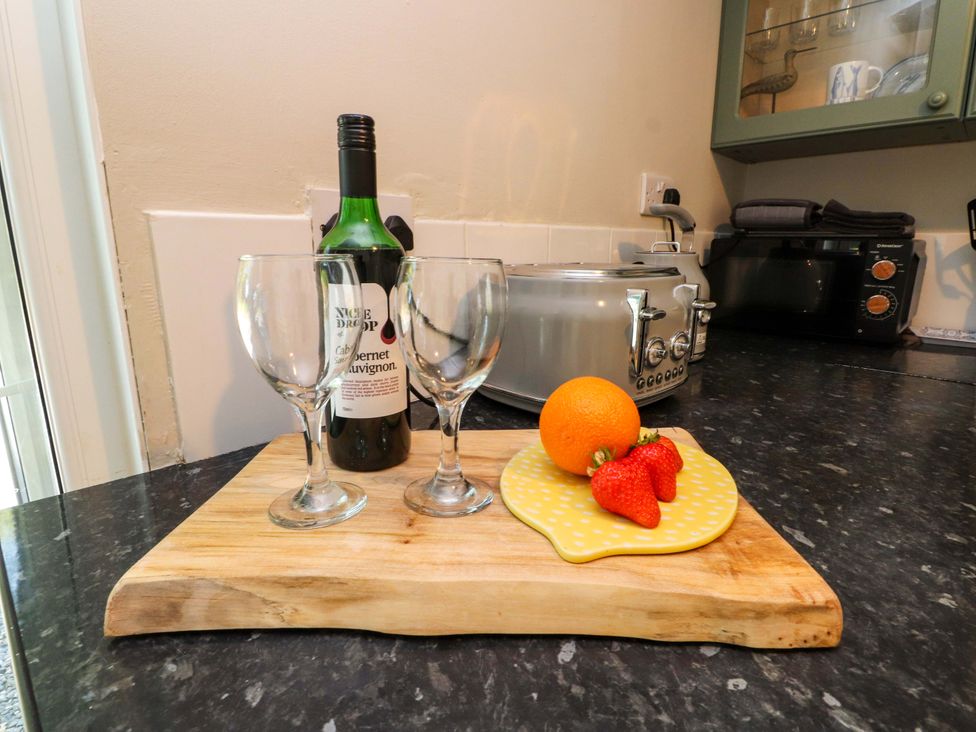 A kitchen with wine glasses and fruit on a cutting board at Woodman's Lodge Llanallgo near Moelfre