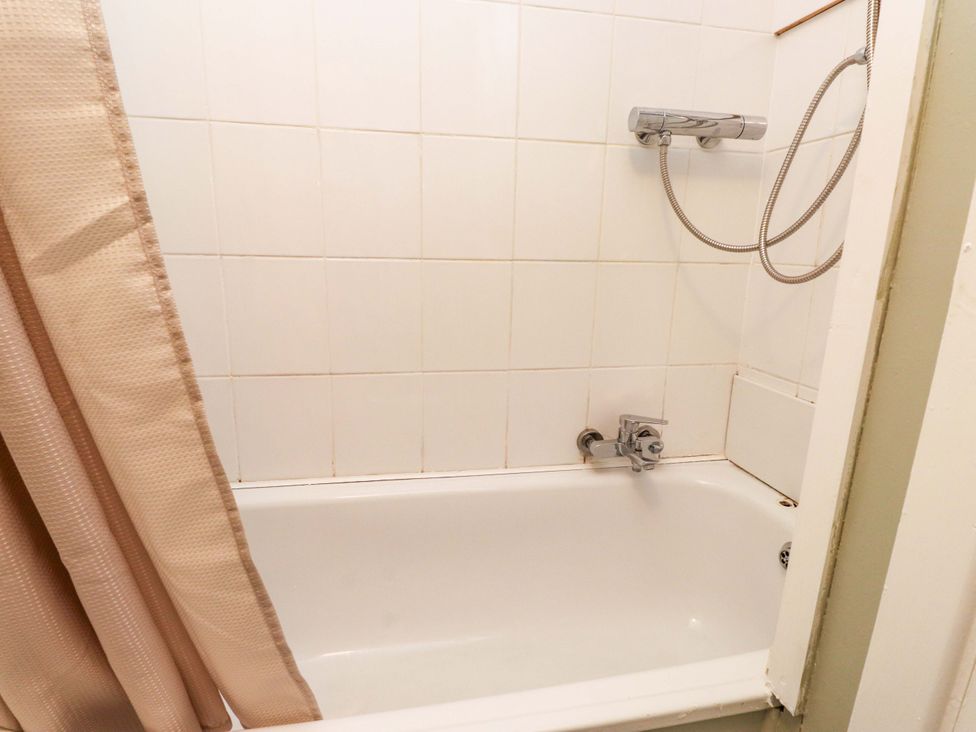 A bathtub with a showerhead and curtain at Woodman's Lodge in Llanallgo near Moelfre