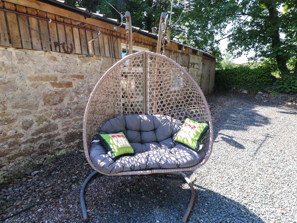 A hanging chair with cushions in an outdoor area at Woodman's Lodge Llanallgo near Moelfre