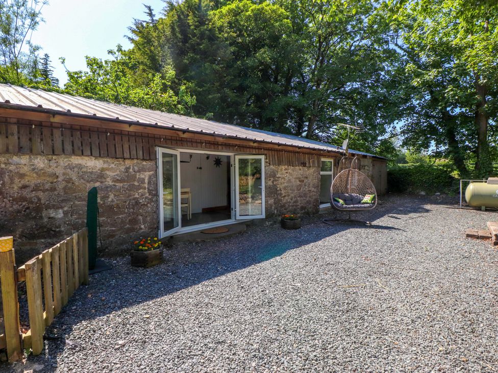 An outdoor area with a building, gravel, and a hanging chair at Woodman's Lodge in Llanallgo near Moelfre