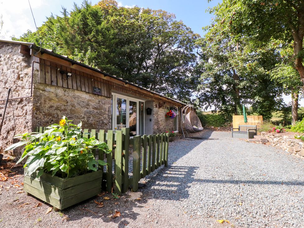 An outdoor area with a stone building and garden features at Woodman's Lodge Llanallgo near Moelfre