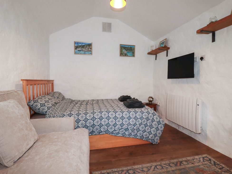 A bedroom with a bed, sofa, and television at Primrose Cottage in Redruth