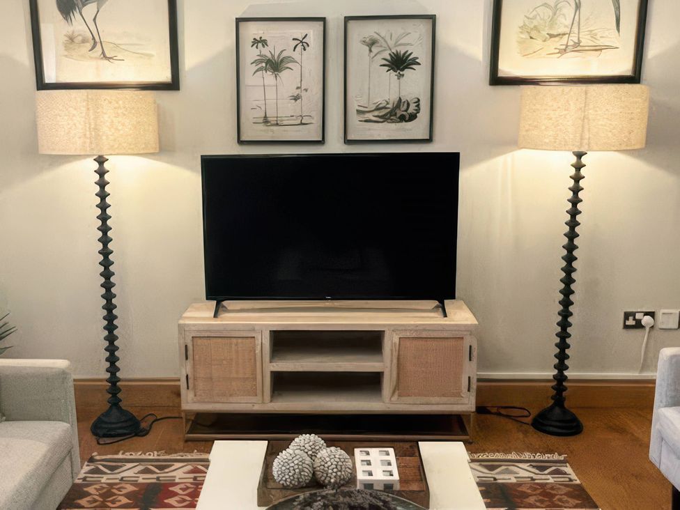 A living room with a TV on a stand and two floor lamps at The Lady Rothschild Stables in Peterborough