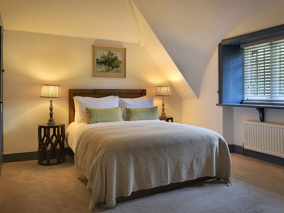 A bedroom with a bed, nightstand, and window at Home Farm Cottage in Peterborough