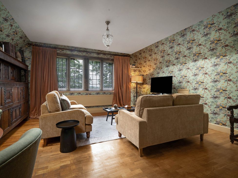 A living room with a sofa, armchair, and television at Rubens Rooms in Peterborough