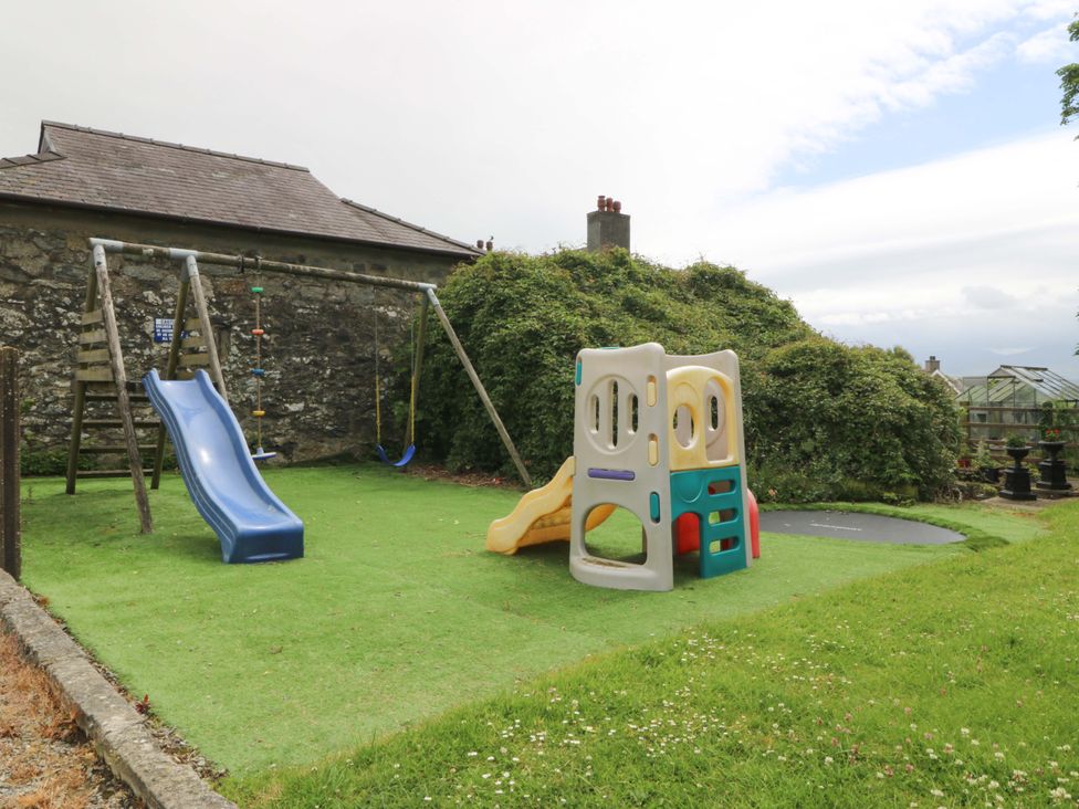 An outdoor play area with a slide, swing, and playhouse at Cil Y Coed in Star near Llanfairpwllgwyngyll