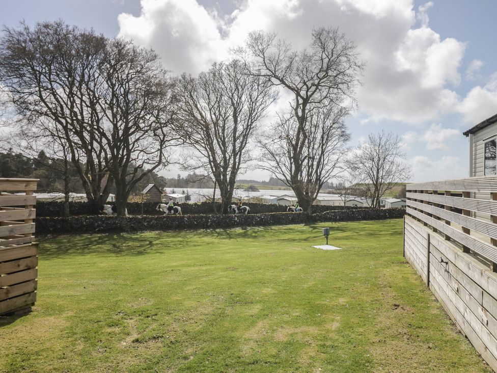 A garden with trees and a stone wall at Standard Caravan at Three Lochs Holiday Park, Newton Stewart