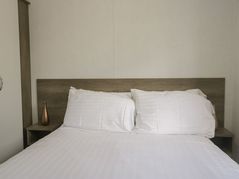 A bed with pillows and a vase on the nightstand at Standard Caravan at Three Lochs Holiday Park, Newton Stewart