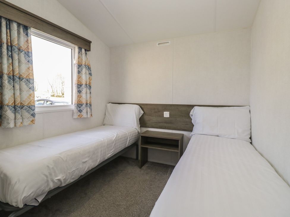 A bedroom with two beds and a window at Standard Caravan at Three Lochs Holiday Park in Newton Stewart