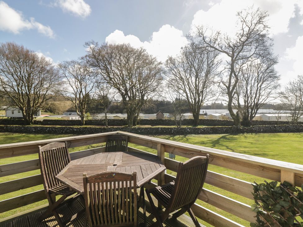 A deck with a table and chairs overlooking caravans at Standard Caravan at Three Lochs Holiday Park in Newton Stewart