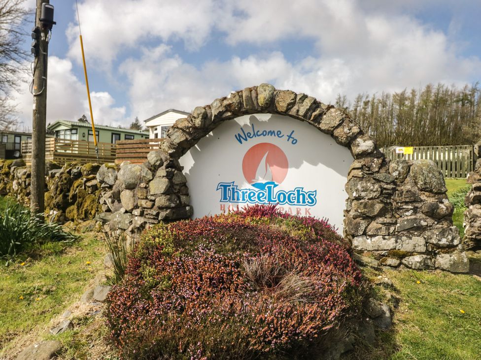 A welcome sign with stone wall and grass at Standard Caravan at Three Lochs Holiday Park in Newton Stewart