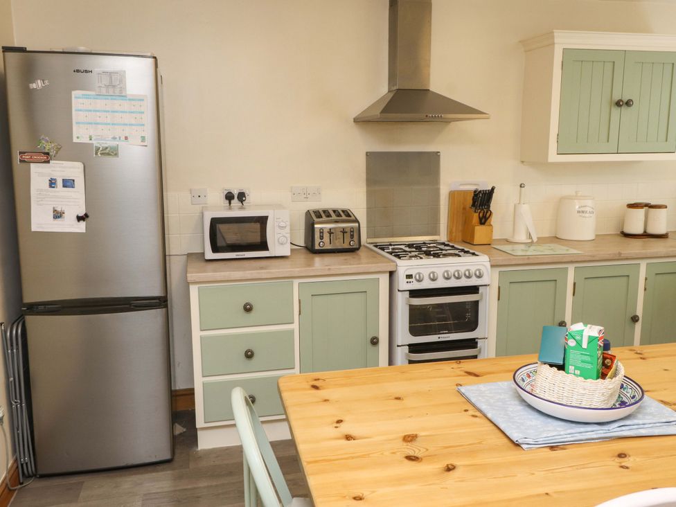 A kitchen with a fridge, stove, and dining table at 2 Bryn Eglwys Prenteg