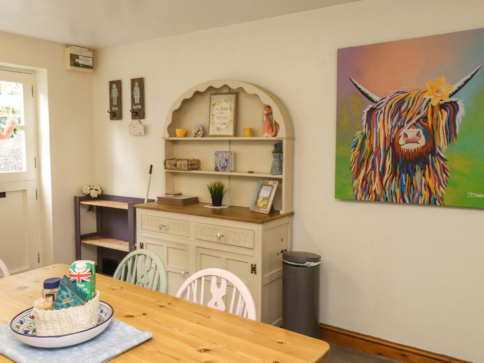 A dining room with a wooden table and a shelf holding decorative items at 2 Bryn Eglwys Prenteg
