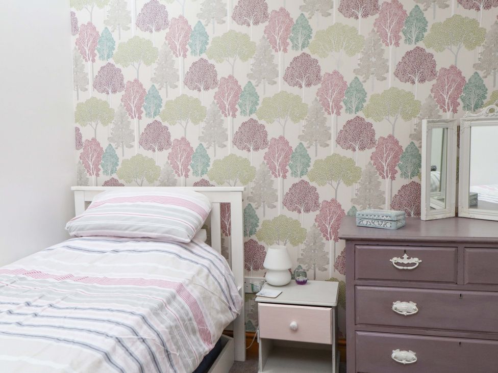A bedroom with a bed, bedside table, lamp and drawer chest at 2 Bryn Eglwys in Prenteg