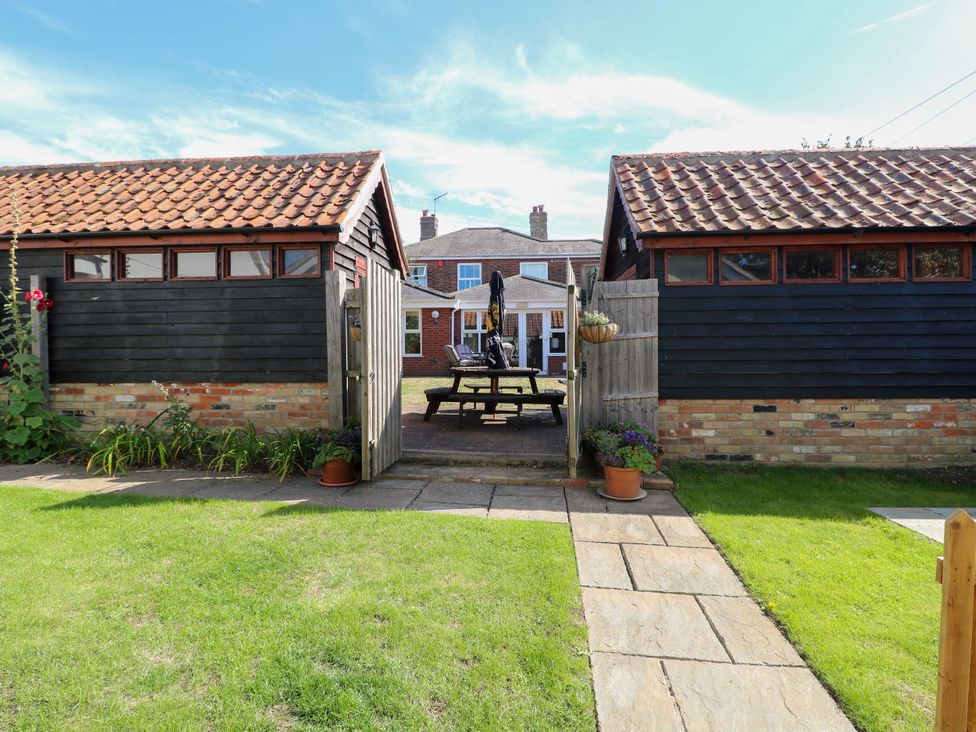 A garden view with a table and chairs between two sheds at The Mill House Gardens Oulton Broad