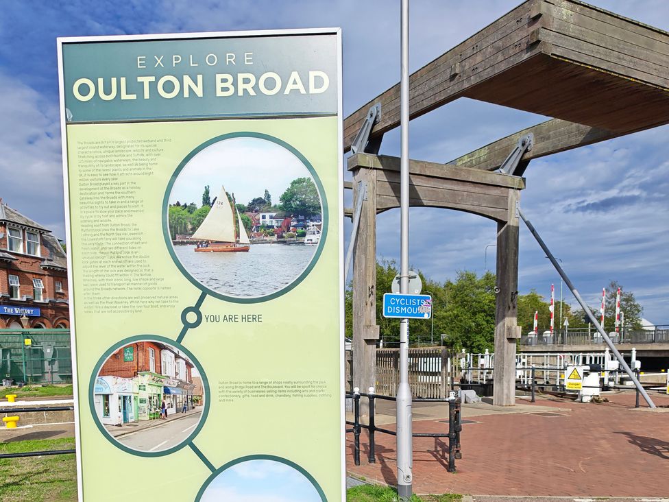 An information board about Oulton Broad with a wooden structure and a sailboat in the background at The Mill House Gardens Oulton Broad