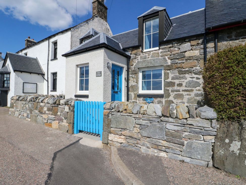 A house with a stone wall and blue gate at Post Cottage in Arisaig
