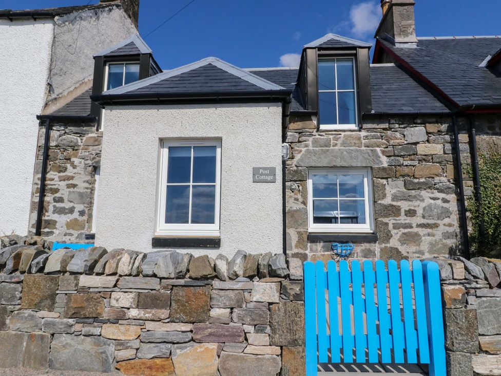 A house with a stone wall and blue gate at Post Cottage in Arisaig