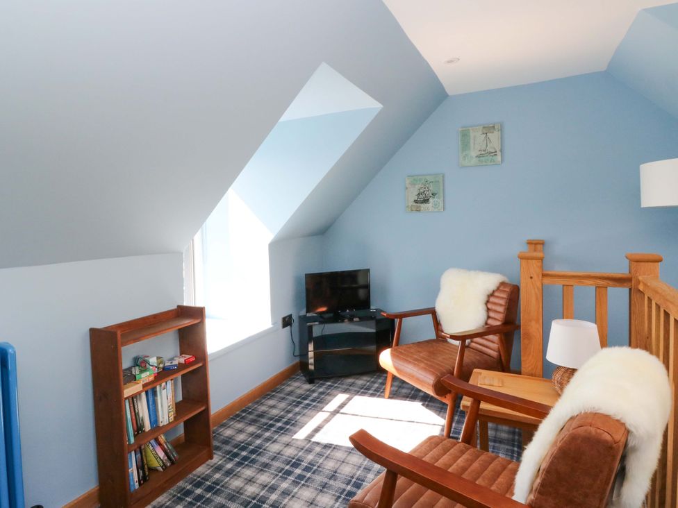A snug with a bookshelf and two chairs at Post Cottage in Arisaig